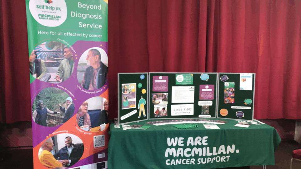 Image of the Self Help UK stand at event, with pull-up banner and table of resources and leaflets